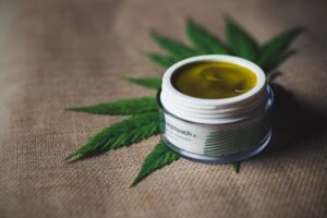 Open jar of green balm beside cannabis leaves