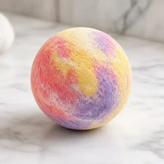 A round, multicoloured bath bomb on a marble bathroom surface